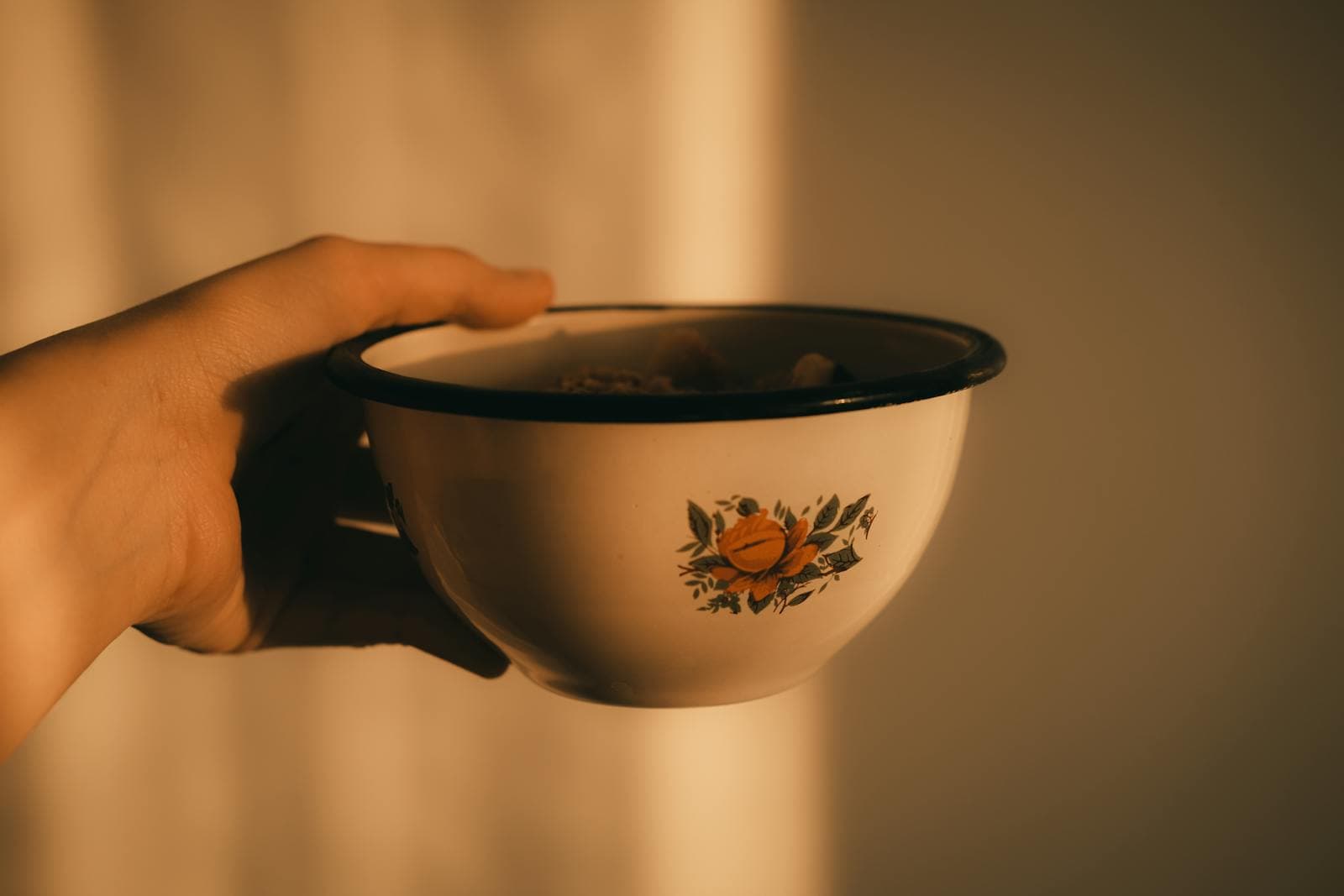 A hand holds out a warm, comforting bowl of soup bathed in soft golden light.